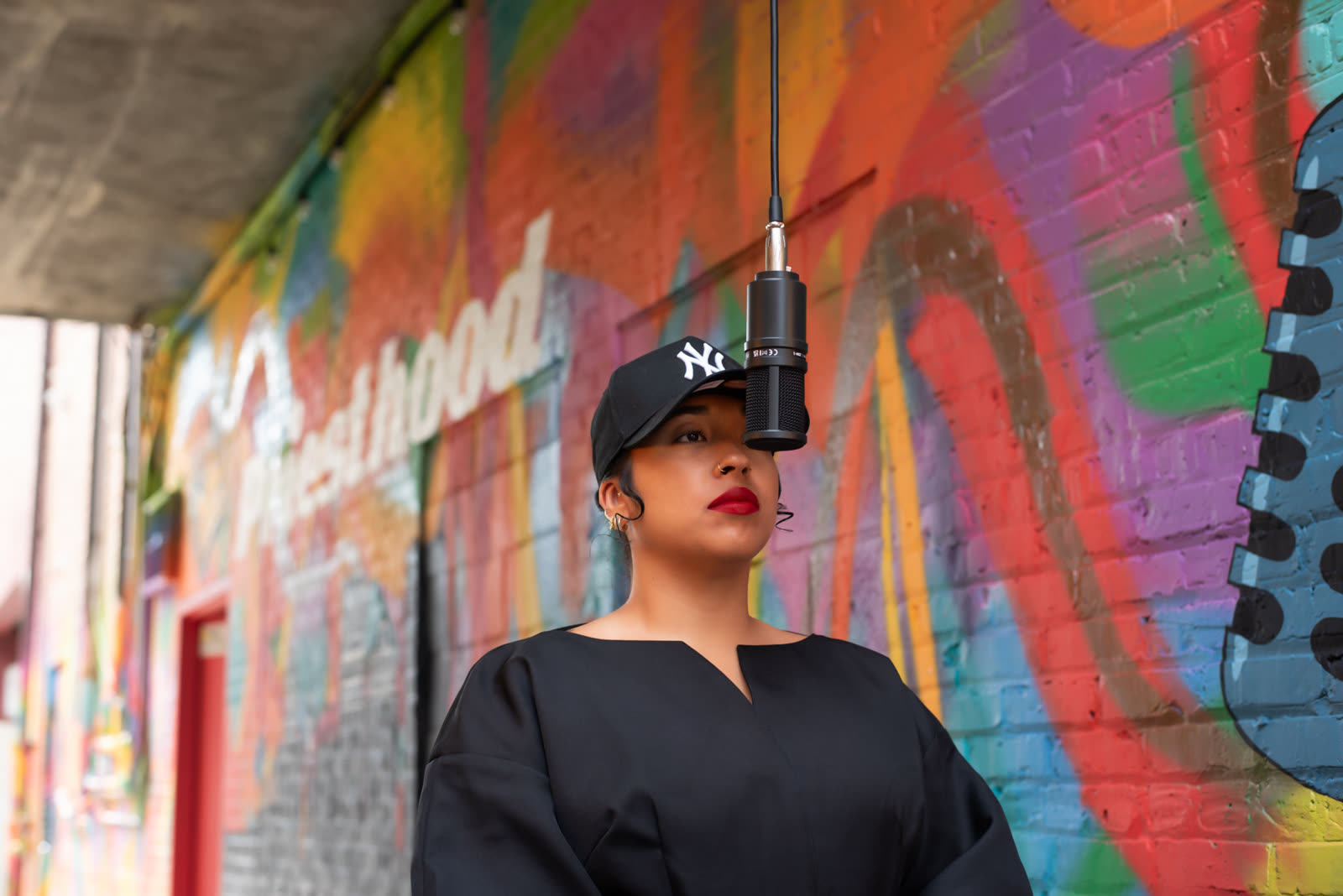 Bella Veronica looking up past a hanging studio microphone in front of a mural.