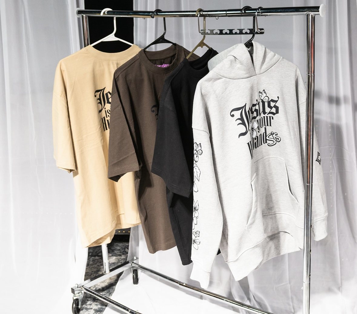 Tan, brown and black Jesus Is Your Husband, Sis tees on a rack.