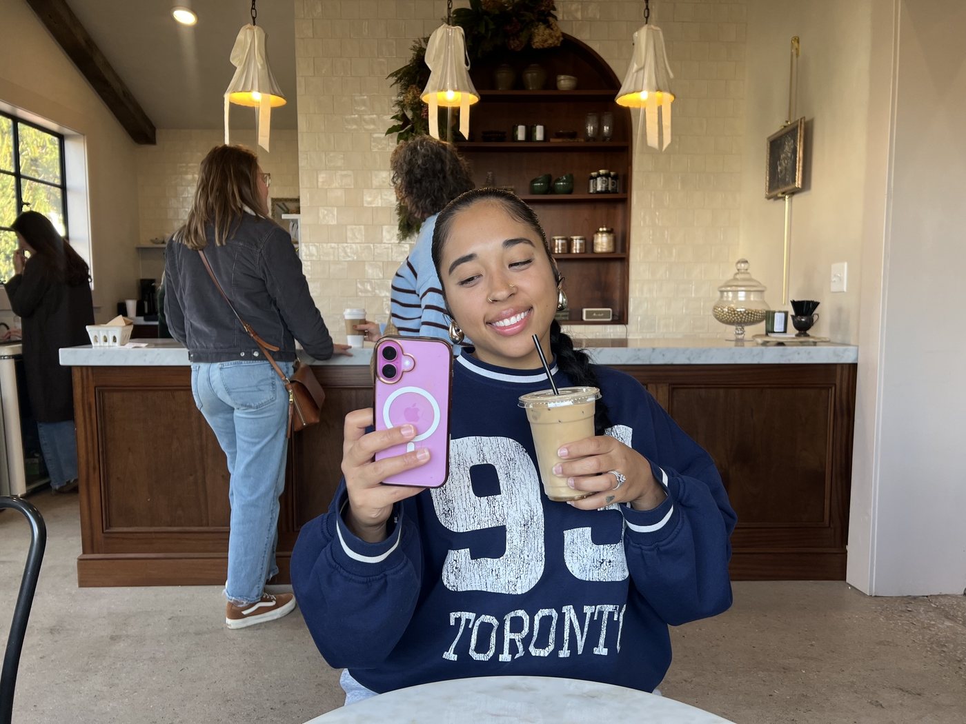 A woman smiling over an iced coffee at the counter of a coffee shop.