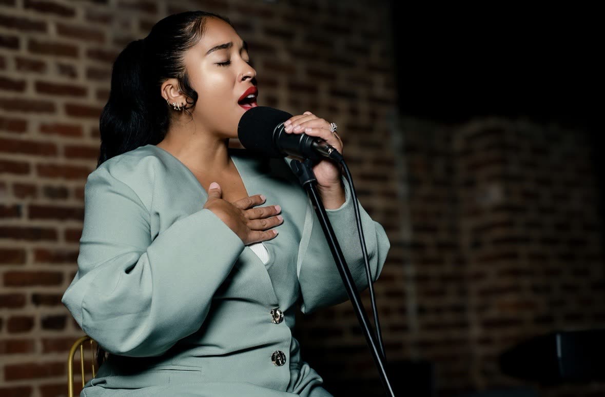 Bella Veronica singing with one hand on her chest.